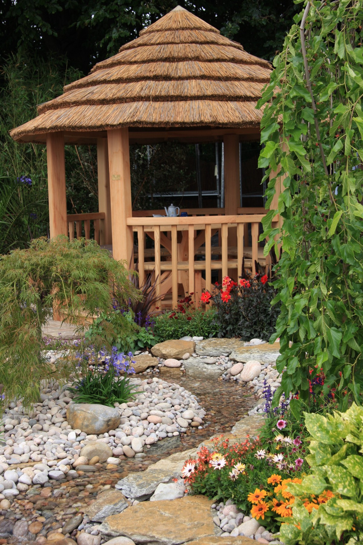 Thatched gazebo with pebble path and pond