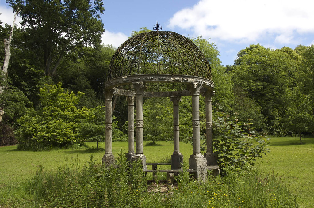 Old iron gazebo with climbers on the metal roof and columns
