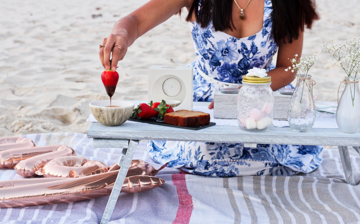 A woman on a beach picnic holding a chocolate-dipped strawberry