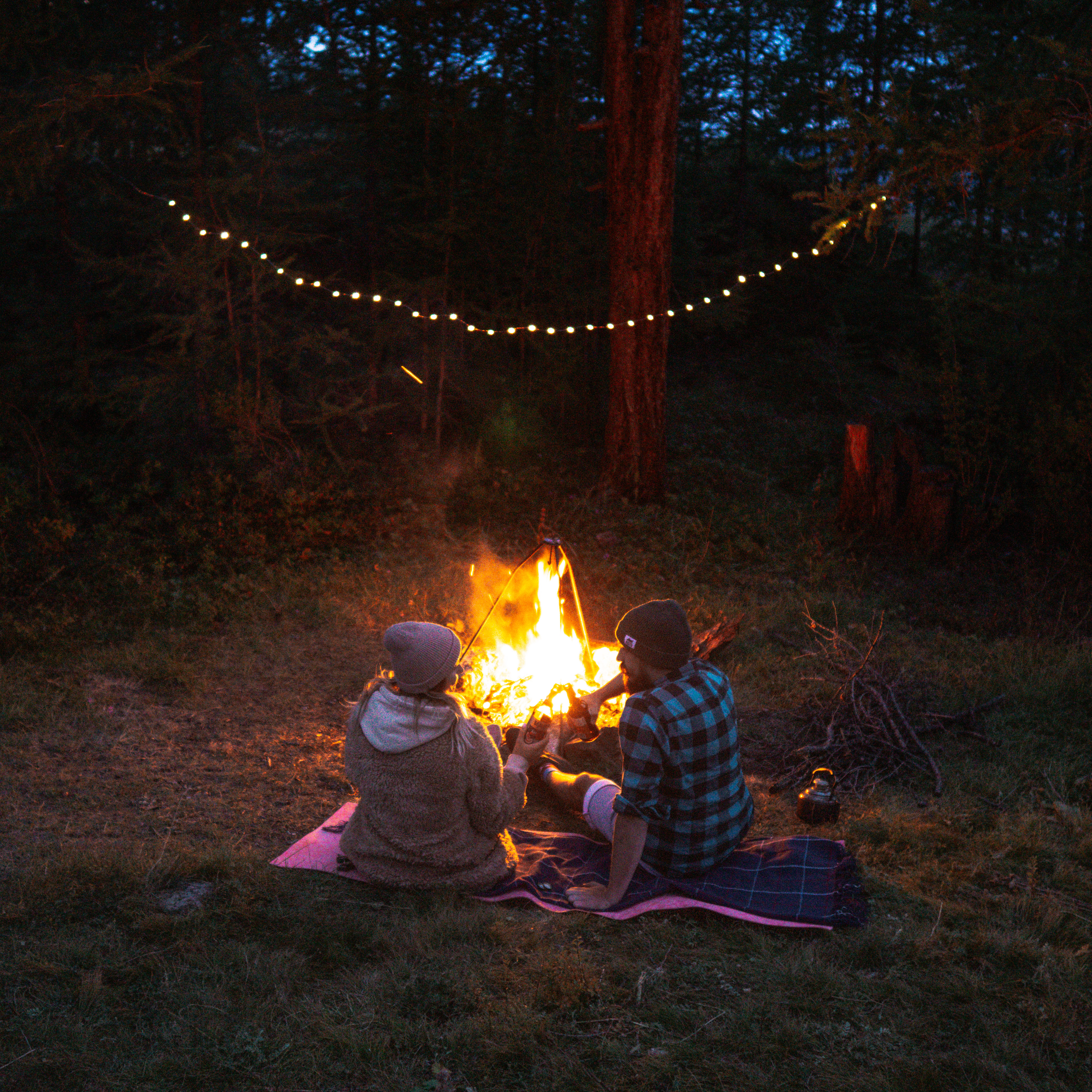Man and woman sitting on ground near bonfire during nighttime