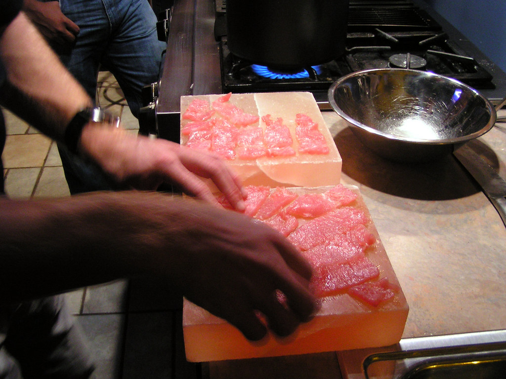 A person putting slices of sashimi on a Himalayan salt plank
