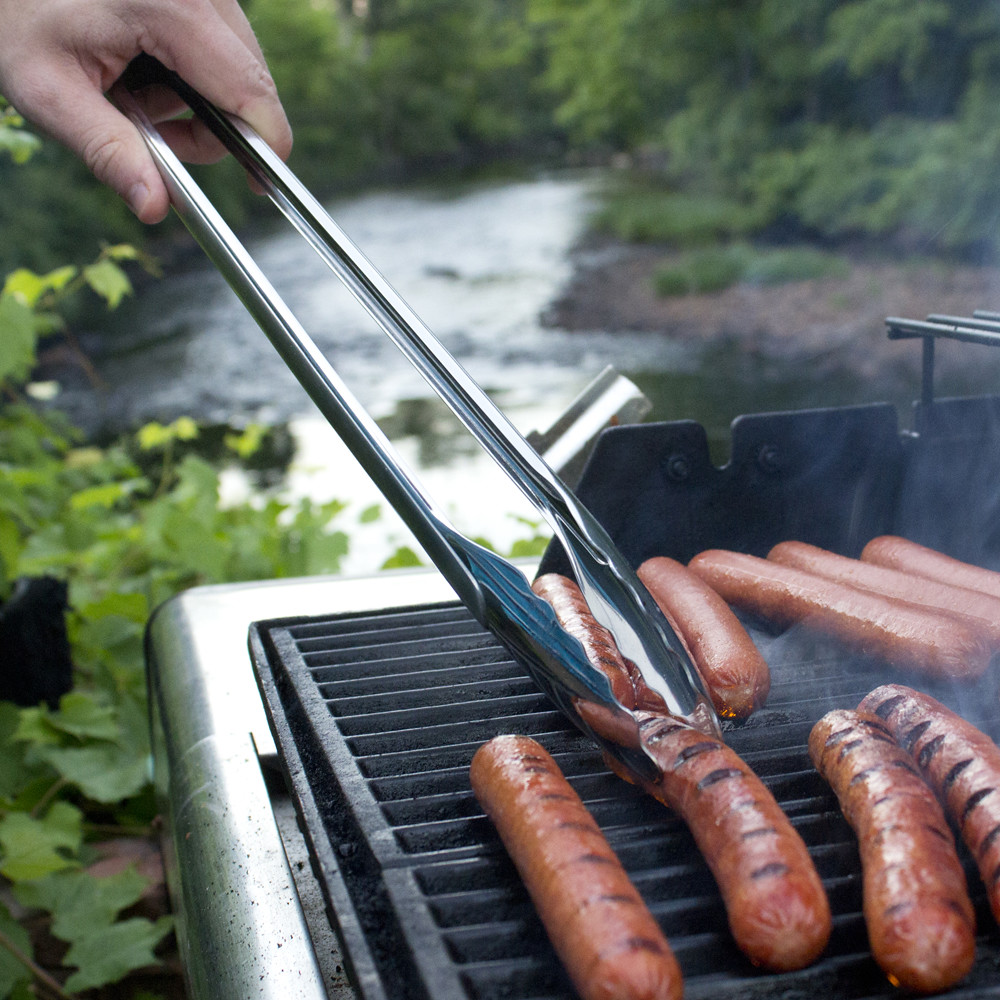 A person holding a tong for the sausages on the grill