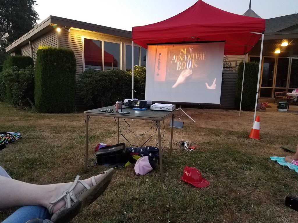 Garden movie night setup with a white projector screen, projector, and red tent 