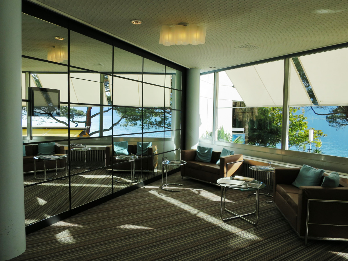 A garden room with a mirror wall on the left side and a view of the ocean on the right open windows.