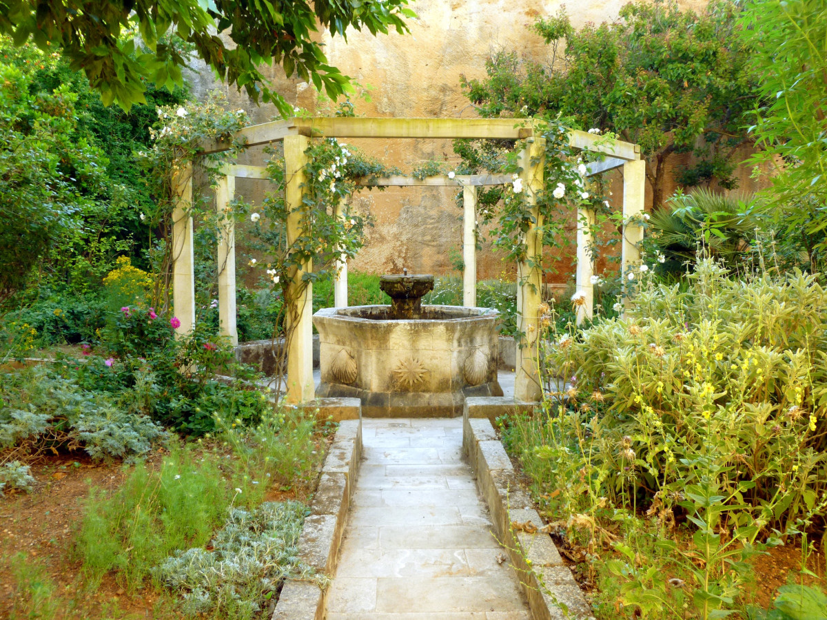 Stone garden fountain inside an open wooden pergola with climbing plants