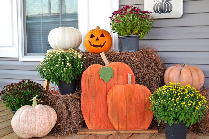 Fall decor on porch, featuring hay bales, Chrysanthemums, and pumpkins.