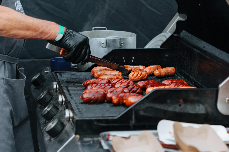 A person grilling sausages on a gas BBQ.