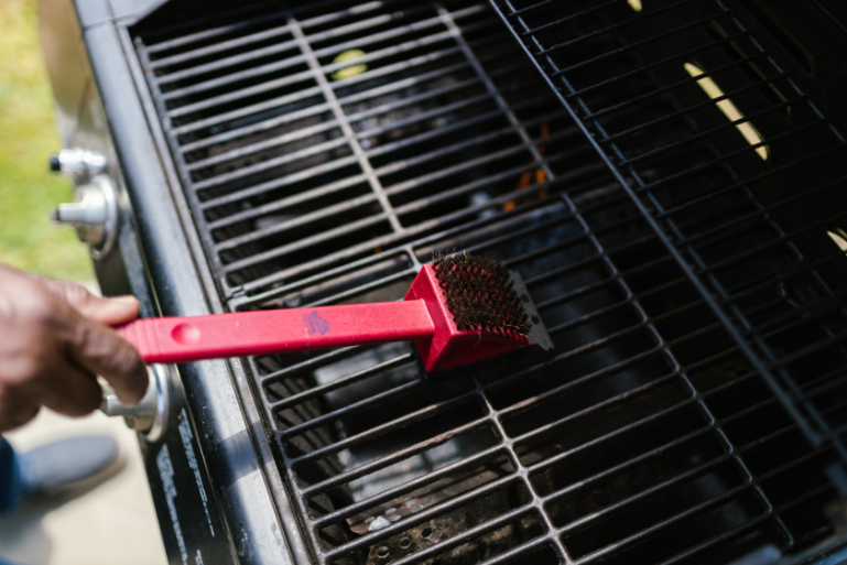 A person holding a wire brush while cleaning the gas BBQ grate