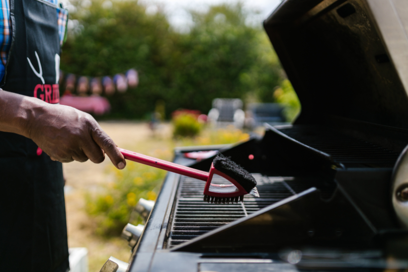 A person cleaning the BBQ grill surface with a brush