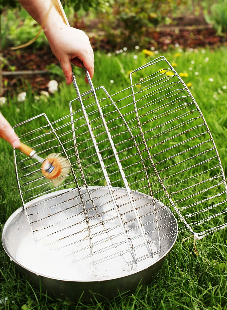 A person cleaning the BBQ grill surface with a brush and water and soap solution