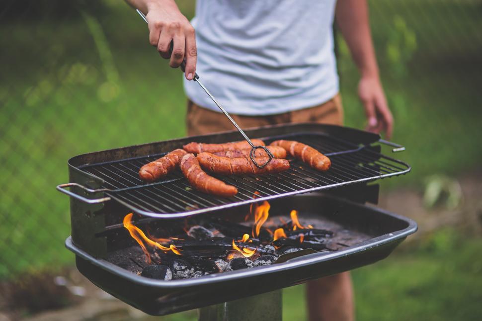 A person grilling sausages on a charcoal BBQ