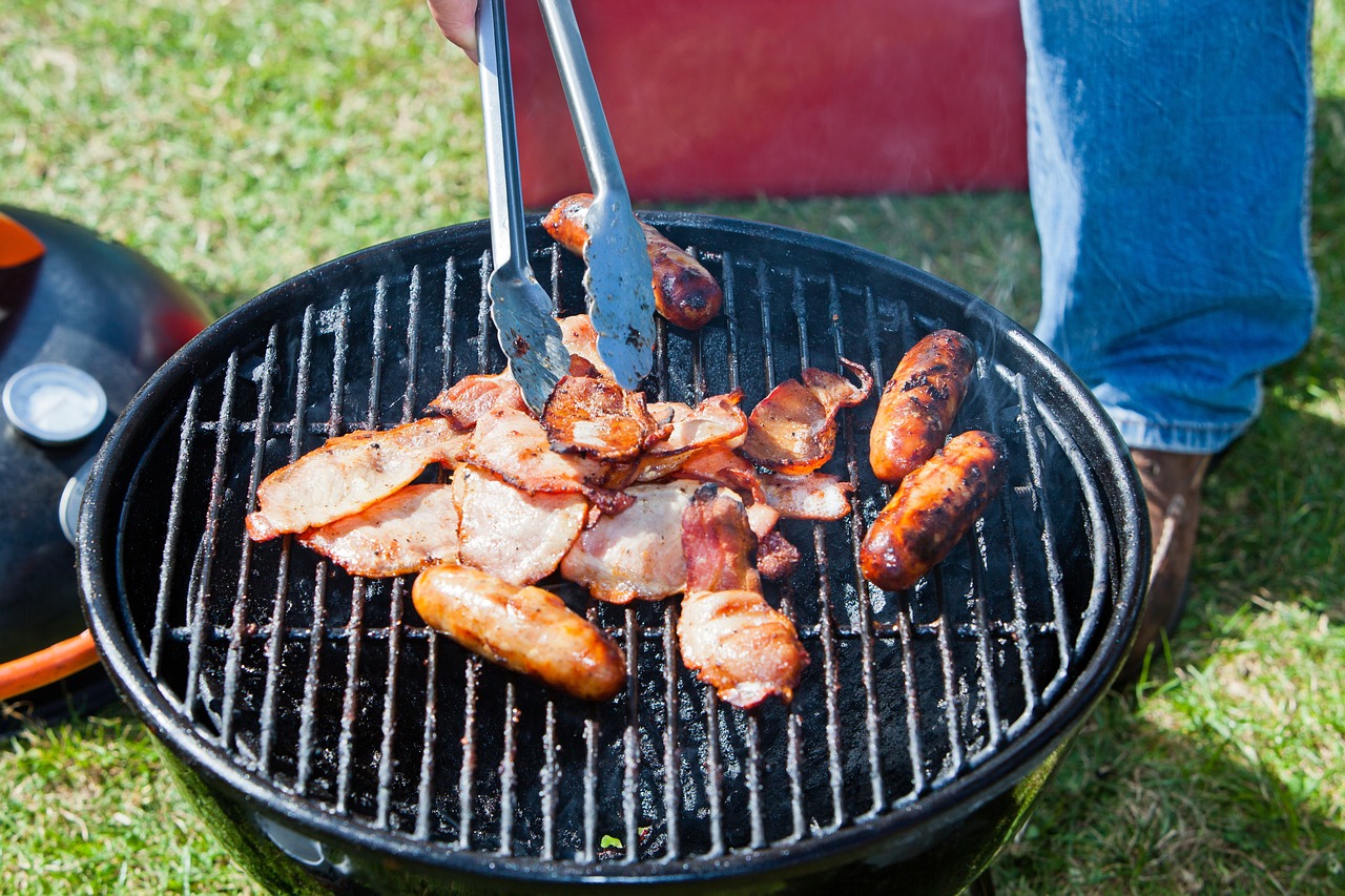 Bacon and sausages being grilling on a portable charcoal BBQ