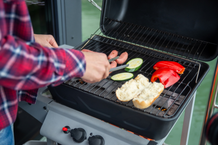 A person grilling sausages and veggies on a portable BBQ