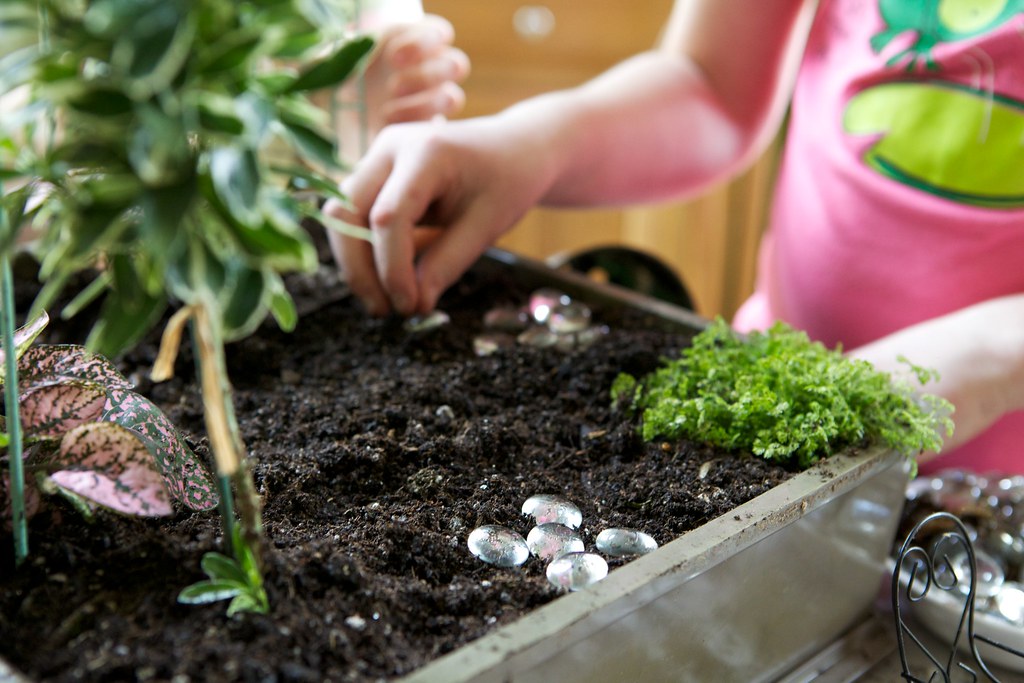 Child’s small hand carefully placing pebbles in a charming fairy garden.