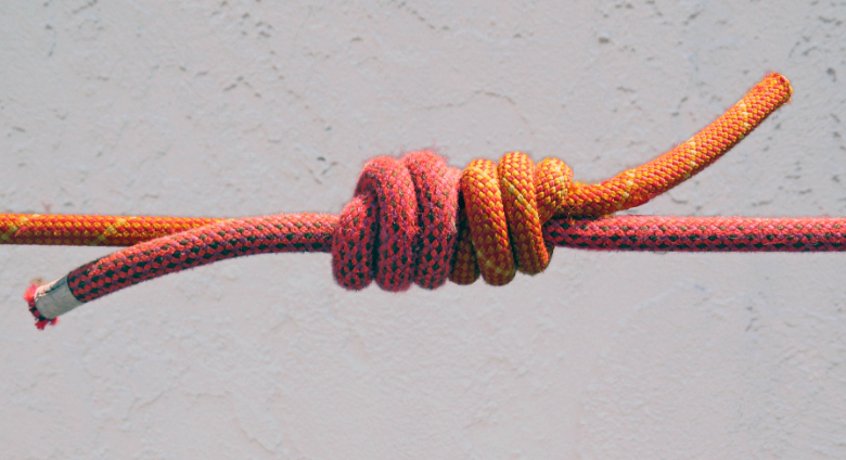 A close-up of a red and yellow rope tied into a fisherman’s knot, secured against a light-colored background.