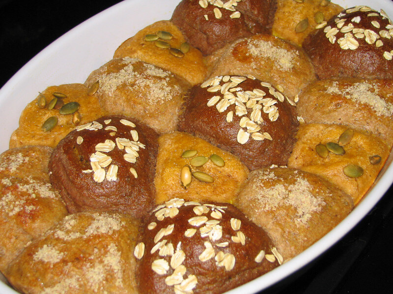 A close-up image of assorted bread rolls in a baking dish, topped with oats, pumpkin seeds, and brown sugar.