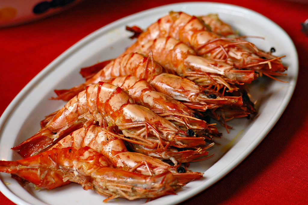 A plate of grilled shrimp served with shells intact, neatly arranged on a white dish, ready to be eaten.