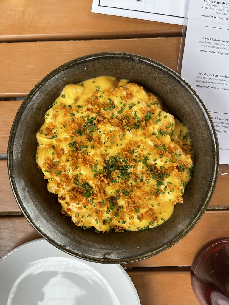 A bowl of creamy mac and cheese topped with crispy breadcrumbs and garnished with chopped chives, served on a table.