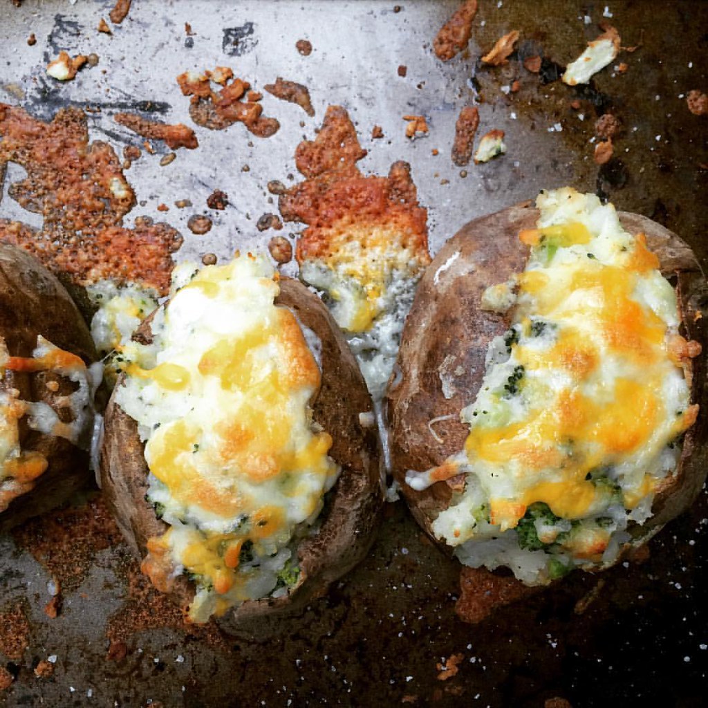 Twice-baked potatoes stuffed with mashed potato, broccoli, and melted cheese, served on a baking tray with crispy cheese bits.