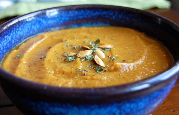 A bowl of creamy pumpkin soup garnished with roasted pumpkin seeds and herbs, served in a blue ceramic bowl.