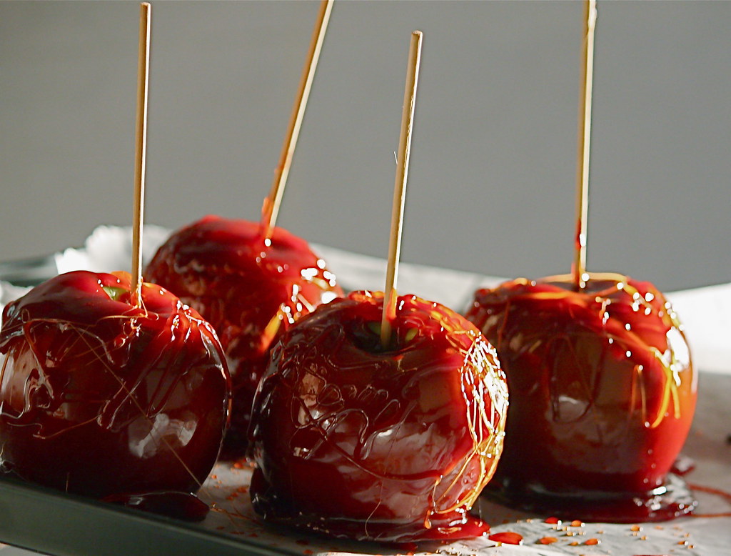 Four shiny red toffee apples on sticks placed on a tray, coated with a thin layer of caramelised sugar.