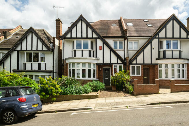 A row of Tudor-style terraced houses with black timber framing, bay windows, and small front gardens with greenery along a paved sidewalk and parked car on the street.