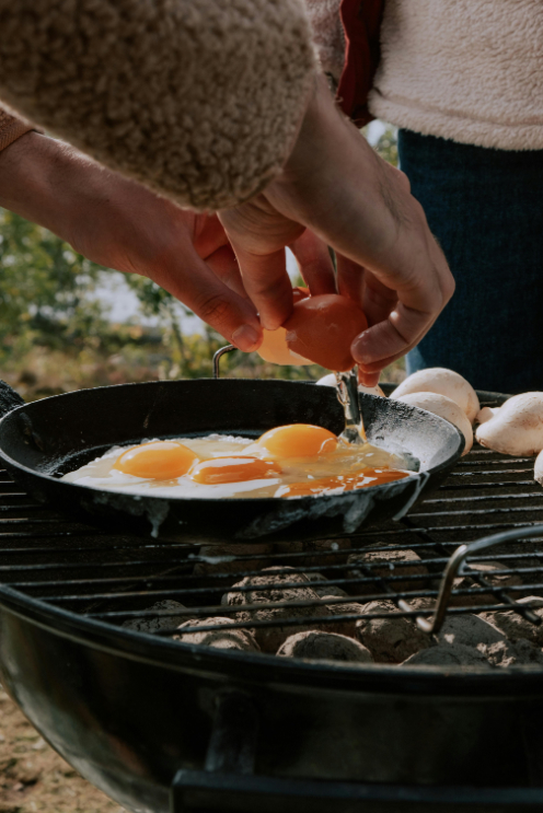 A person frying eggs in a cast-iron pan on the BBQ.