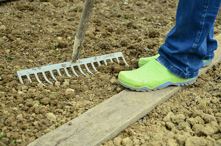 A brown rake resting on the soil, ready for use in the garden.