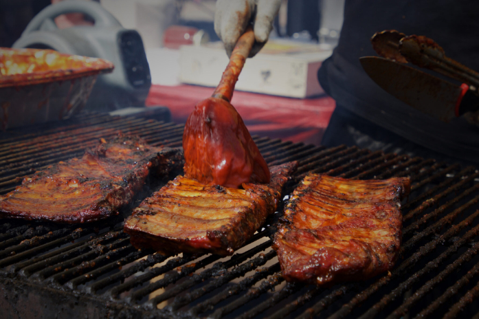 Pork ribs on a grill being brushed with sauce.