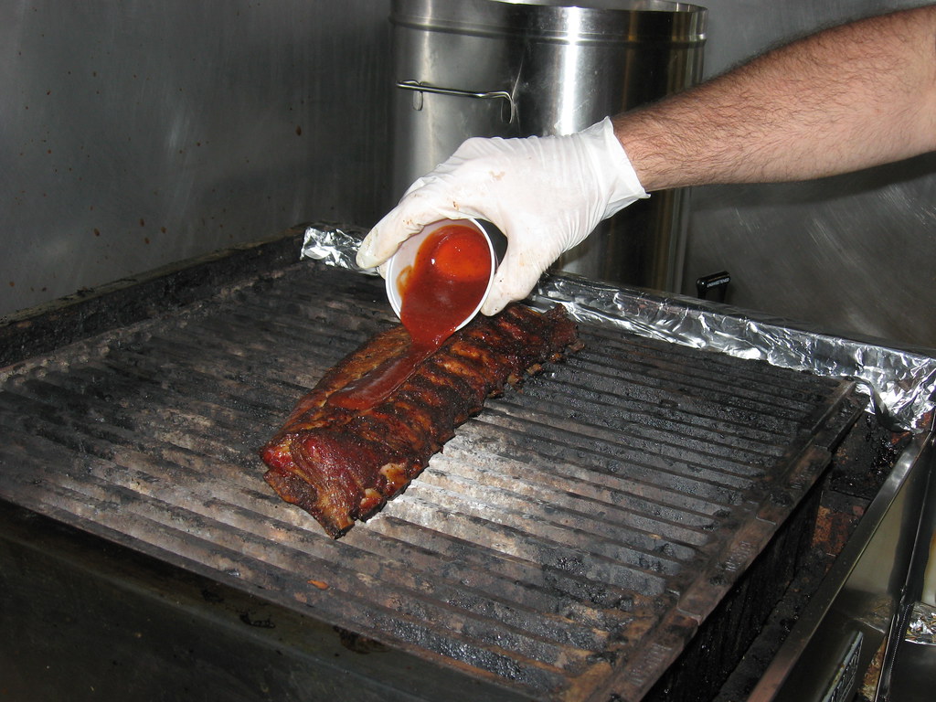 A Central-style BBQ rib on the grill with sauce being poured from a small cup.