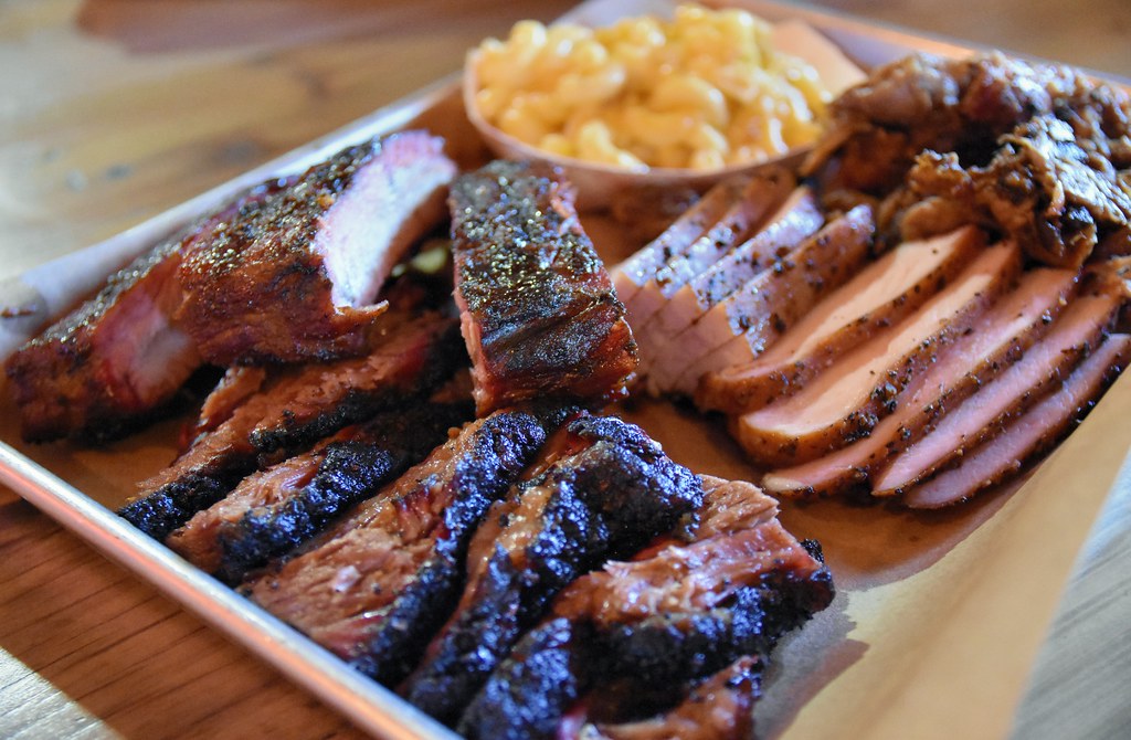 Texas BBQ platter featuring moist brisket, pulled pork, turkey, and ribs, served with mac and cheese.