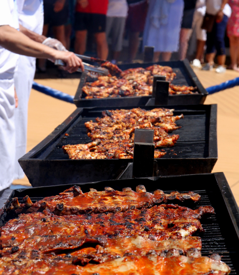 Three barbecue grills by the pool with a man grilling food.