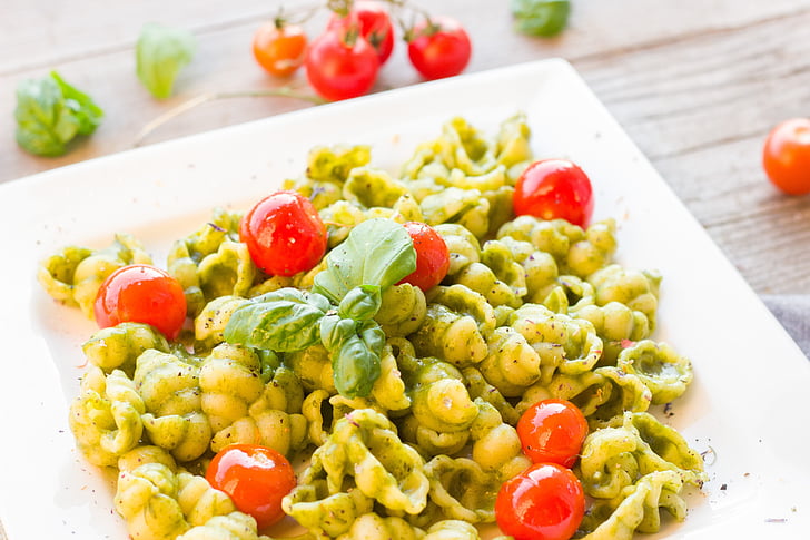 Cooked pasta with pesto sauce, cherry tomatoes and herb on a white ceramic plate.