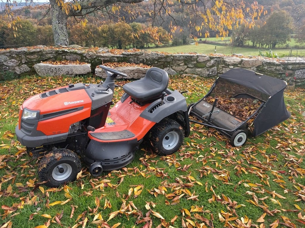 Tractor lawn mower parked on grass with leaves around it.
